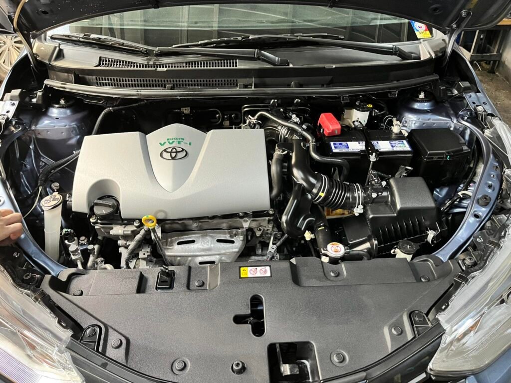 Overhead view of a clean, modern car engine bay with the hood open, showing the engine cover and battery.